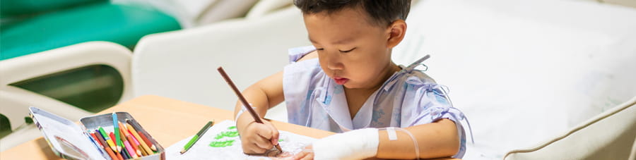 Boy patient coloring in hospital bed.