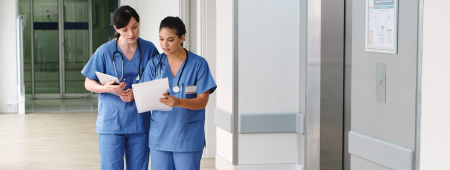 Two nurses discussing a file in the hallway.