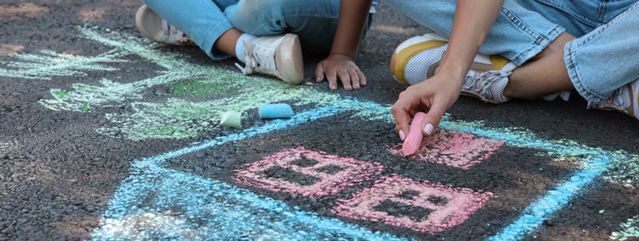 Children drawing a house in bright chalk on blacktop.