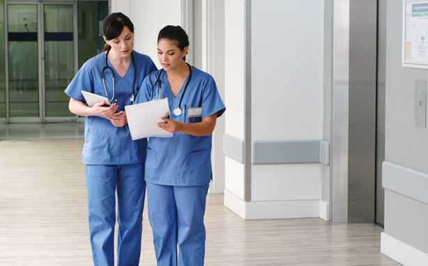 Two nurses discussing a file in the hallway.