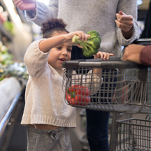 Young child puts broccoli in grocery basket.